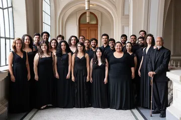 Os coralistas da Academia de Música estão posicionados em uma escada da Sala São Paulo. Todos vestem roupas pretas e sorriem.