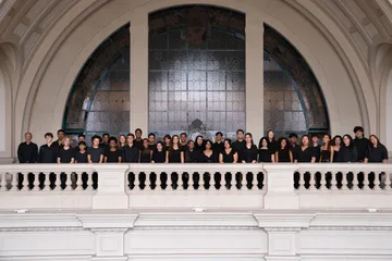 Alunos do coro juvenil, vestindo roupas pretas, cantam no palco da Sala São Paulo segurando pastas com as partituras nas mãos.