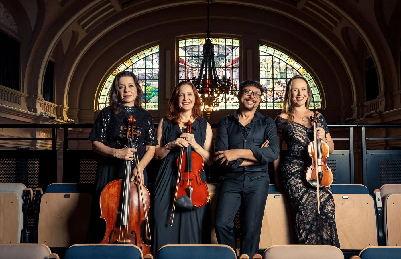 A imagem mostra os quatro integrantes do Quarteto Poesis na plateia da Estação Motiva Cultural, com o vitral do espaço ao fundo.