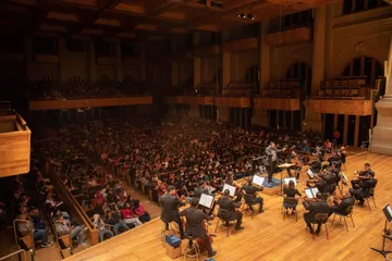 Concerto na Sala São Paulo, com palco e platéia a vista. O público é composto apenas por jovens e crianças, no palco, temos um grupo artístico tocando.