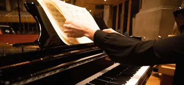 Pessoa branca folheando uma partitura colocada no suporte do piano